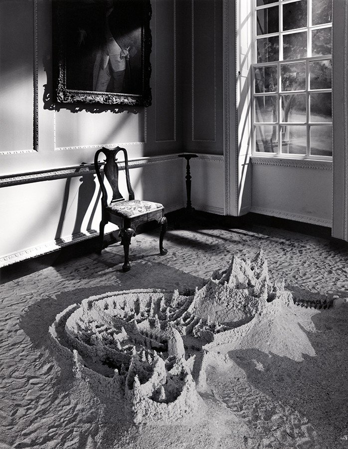 Photomontage noir et blanc de Jerry UELSMANN. La photographie montre un château de sable dans un intérieur.